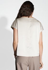 Top satin beige chiaro con maniche corte, taglio dritto e una leggera lucentezza. Abbinato a pantaloni marroni chiari, che mostrano un design semplice ed elegante.