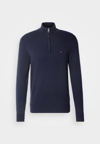 Pull à manches longues bleu marine avec col à fermeture éclair sur le quart et petit logo rouge, blanc et bleu sur la poitrine gauche.