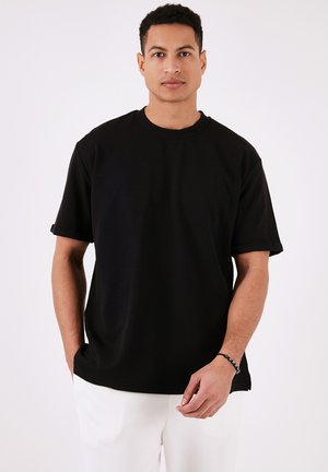 Sort kortærmet t-shirt i en afslappet pasform, lavet af blød bomuld. Har rund hals, oprevne ærmer og en lige kant.