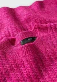 Felroze gebreide trui met ribbels op de kraag en een geweven patroon, met een zwart label waarop "MNG" en "Made in Turkey" staat.