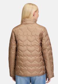 Pikowana kurtka w jasnobrązowym kolorze z sercowymi wzorami. Posiada wysoką kołnierz i długie rękawy, wykonana z gładkiego, matowego materiału.