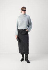 Světle modrý pletený svetr s vysokým límcem, černá denimová maxi sukně a černé kozačky do kolen. Sluneční brýle a malá černá kabelka.