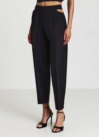 Pantalons noirs taille haute avec découpes latérales, coupe ajustée, texture lisse et jambes fuselées. Associés à des sandales noires à talons avec lanières.