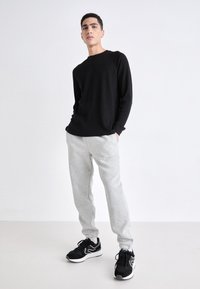 Zwarte lange mouwen shirt, lichtgrijze sweatpants en zwarte sportieve schoenen. De outfit heeft eenvoudige ontwerpen en een ontspannen pasvorm.