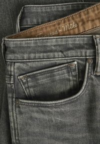 Vaqueros de denim gris oscuro con un corte ajustado, que presentan una etiqueta en la cinturilla de color marrón y costuras en contraste. Incluye un detalle en el bolsillo trasero.