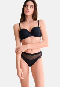 Ensemble de lingerie noire comprenant un soutien-gorge rembourré avec texture à pois et des culottes taille haute assorties avec des accents en dentelle transparente et des bords festonnés.
