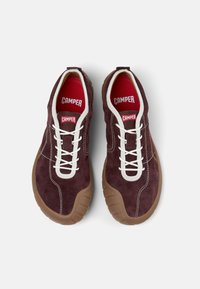 Baskets en suède bordeaux avec des lacets blancs et une semelle en caoutchouc marron clair, arborant le logo "Camper" sur la languette et la semelle intérieure.