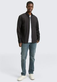 Schwarz gestreifte Hemd mit Knöpfen über einem weißen T-Shirt, kombiniert mit hellblauen Jeans und weißen Sneakern. Keine sichtbaren Muster oder Akzente.