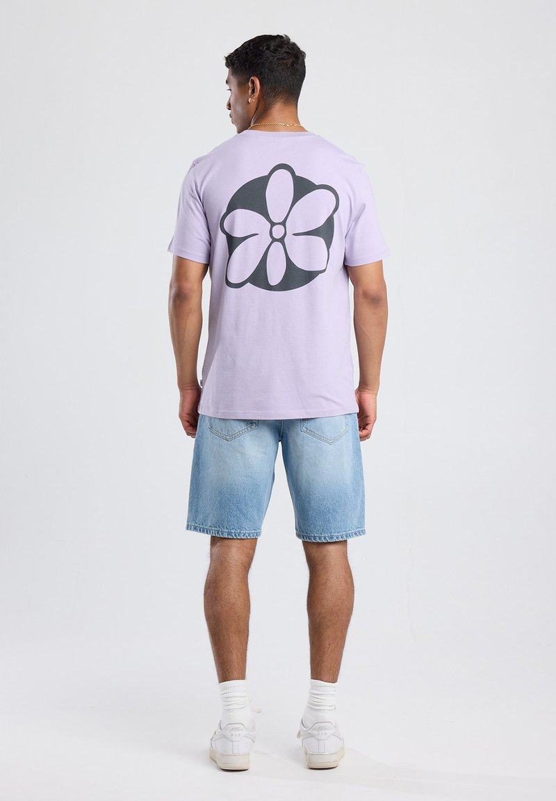 Lila korte mouwen t-shirt met een grote zwarte bloemenprint op de achterkant. Gekocht met lichtblauwe denimshorts en witte sneakers.