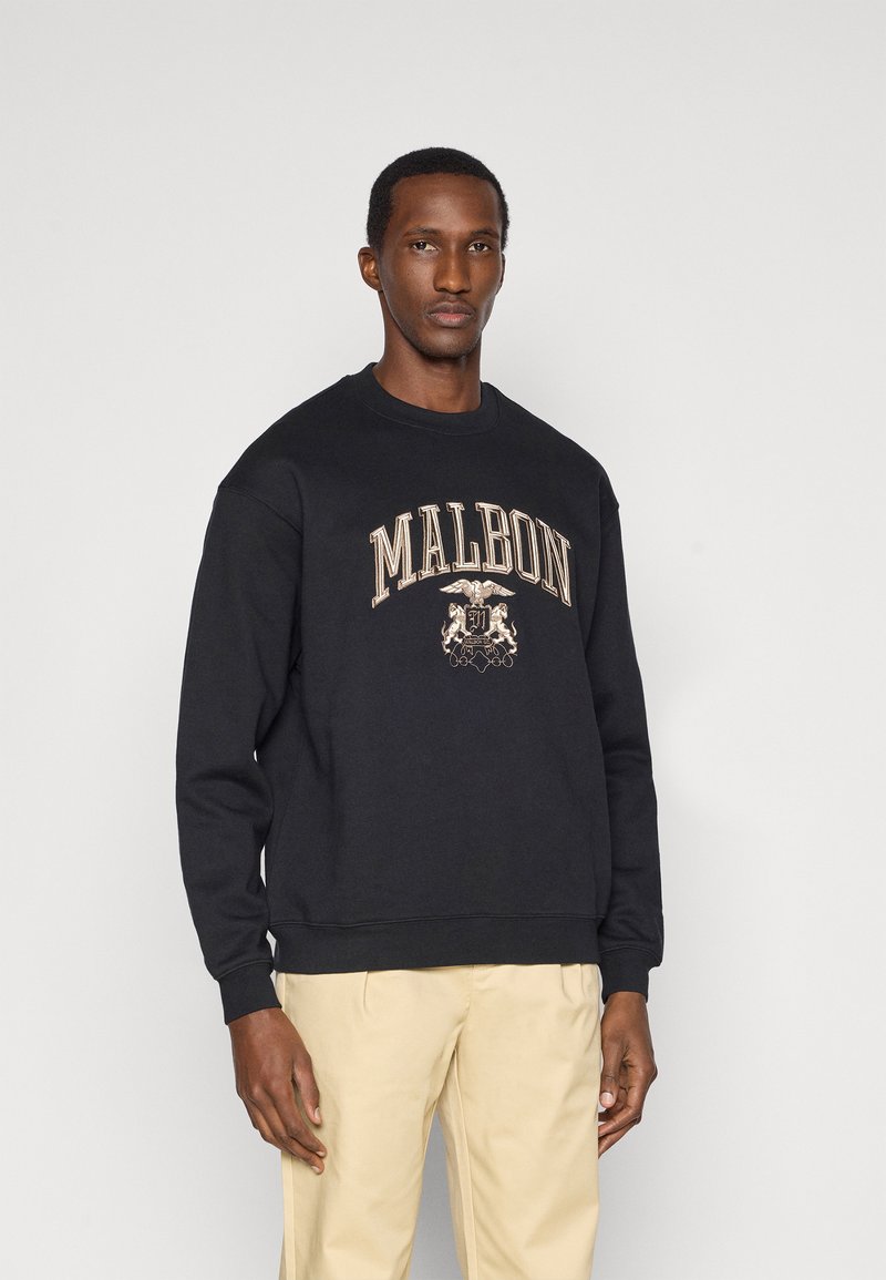 Μαύρο φούτερ με στρογγυλή λαιμόκοψη, που φέρει το "MALBON" σε χρυσή κεντητή γραφή και σχέδιο κρενών. Το μοντέλο το συνδυάζει με μπεζ παντελόνι. Λείος υφασμάτινος χαρακτήρας.