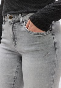 Γκρι τζιν denim με εφαρμοστή σχεδίαση, διακριτικό ξεθώριασμα και μικρή φθορά. Διαθέτει κουμπί και φερμουάρ για κλείσιμο.