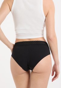 Braguitas negras de algodón con una cinturilla de encaje, con una textura suave y un diseño de talle alto, mostrando la vista trasera y costuras mínimas.