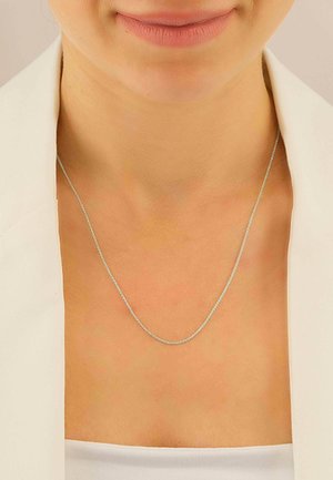 Eine Silberkette, die vor einem hellen Hautton präsentiert wird. Sie zeichnet sich durch ein einfaches, zartes Design mit einer glatten, polierten Oberfläche aus.