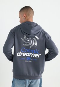 Gray hooded sweatshirt featuring a spiral design and the text "Cosmic dreamer" in blue and white. Soft fabric, casual fit.