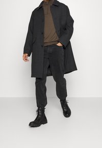 Tmavě šedý vlněný kabát s límcem a knoflíky, přes hnědý rolák. Kombinováno s černými zúženými kalhotami a černými šněrovacími botami.