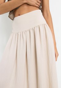 Light beige skirt with a high, elastic waistband and gathered pleats. Made from soft fabric with a smooth texture. A-line silhouette.