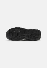 Semelle de chaussure en caoutchouc noir avec des motifs de rainure profonds et larges pour une meilleure adhérence et durabilité, vue par le dessous.