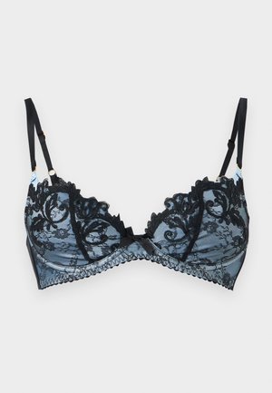 Soutien-gorge balconette en dentelle noire avec broderie florale et bretelles réglables sur fond gris clair.