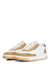 White and tan sneakers with suede and leather materials, contrasting black heel, and white laces. Gold logo on the tongue.