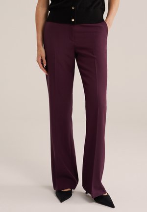 Femme portant un pantalon droit taille haute violet foncé avec poches latérales et des talons noirs à bout pointu.