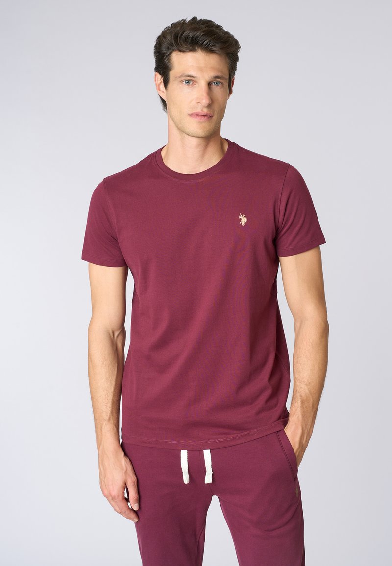 T-shirt corto color marrone scuro in cotone, con colletto rotondo e un piccolo logo ricamato sul lato sinistro del petto. Tessuto morbido.