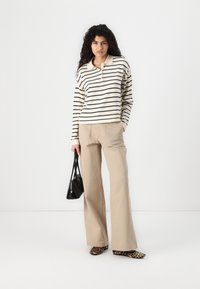 Striped long-sleeve top in cream and black, beige wide-leg pants, black handbag, leopard print shoes; model has curly hair.