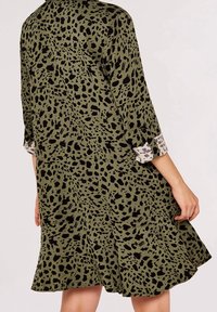Grøn kjole med sort dyreprintmønster, der har en udvidet kant og 3/4-ærmer med et kontrasterende mønstret manchet.