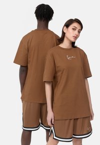 Brown cotton t-shirt with short sleeves and a white logo. Styled with matching brown shorts featuring black and white accents.