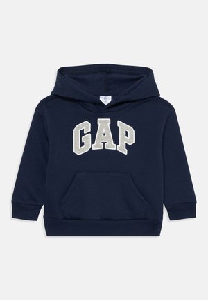Sweat à capuche bleu marine avec une poche avant et de grandes lettres blanches formant GAP sur la poitrine, conçu pour les enfants.