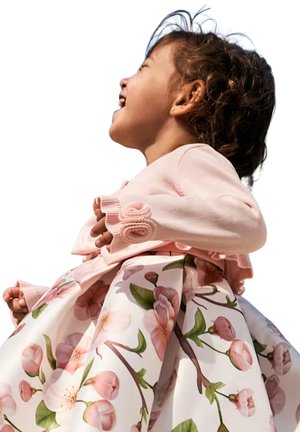 Cardigan rosa chiaro con maniche ruffle e abito a fantasia floreale con fiori rosa in fiore su sfondo bianco.