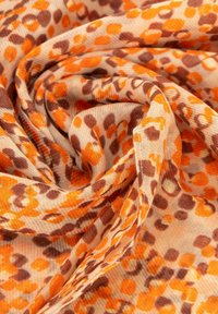 Tejido ligero que presenta una mezcla de manchas naranjas y marrones sobre un fondo beige, con una textura suave y ligeramente transparente.
