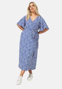 Sininen kietaisumekko, jossa on valkoinen abstrakti kuvio, lyhyet hulmuavat hihat, sidottu vyötärö ja midi-pituus; yhdistetty valkoisiin lenkkareihin.