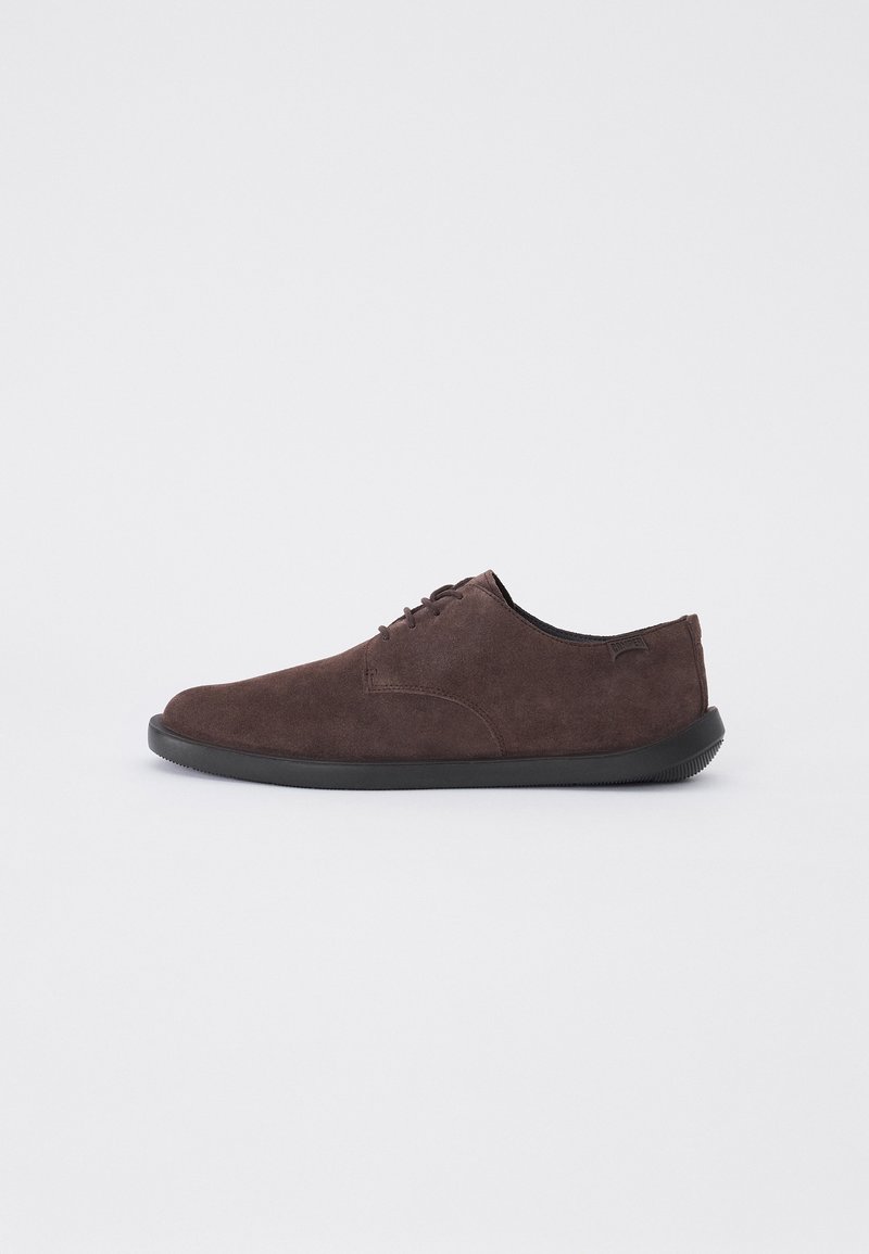 Chaussure en suede marron foncé à lacets avec semelle noire, profil bas et couture minimale, présentée en vue latérale gauche sur fond blanc.