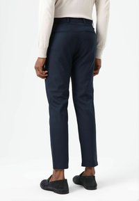 Marineblauwe, op maat gemaakte broek van een gladde stof, met een slanke pasvorm, twee achterzakken en een nette zoom. Gecombineerd met donkere loafers.