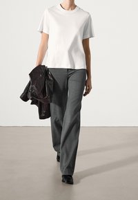 White short-sleeve t-shirt, gray tailored trousers, and a dark leather jacket, with black footwear, shown on a model walking.