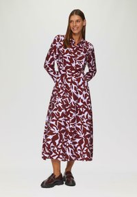 Długa burgundowa sukienka w geometryczny biały wzór. Posiada długie rękawy, kołnierzyk i wcięcie w talii. Noszona z ciemnymi mokasynami.