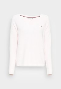 Pull tricoté rose clair avec un col en V, des poignets côtelés et des détails sur les côtés. Présente un petit logo sur la poitrine gauche. Tissu texturé.