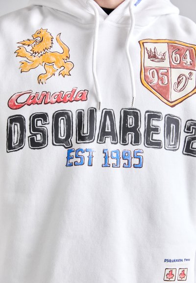 Witte hoodie met kleurrijke graphics: een oranje leeuw, "Canada", "DSQUARED2" en een schild met cijfers. Zacht materiaal met een relaxte pasvorm.