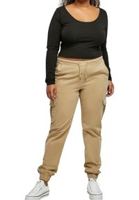 Crop top noir à manches longues associé à un pantalon cargo kaki à cordon avec poignets élastiques et poches latérales, porté avec des baskets blanches.
