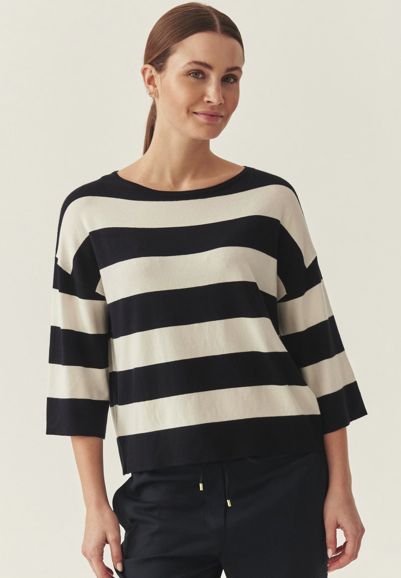 Pull rayé marine et ivoire, large encolure bateau, manches trois-quarts, texture douce, coupe décontractée, agrémenté d'accents métalliques dorés.