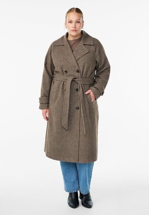 Brown checked double-breasted trench coat with a tie belt, featuring large lapels and side pockets, worn over blue wide-leg jeans and ankle boots.