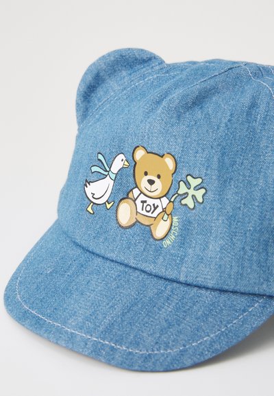 Gorra de mezclilla azul con gráfico de oso y pato. Presenta un oso que lleva una camiseta con la palabra "TOY" y una hoja verde, orejas redondeadas y visera cosida.