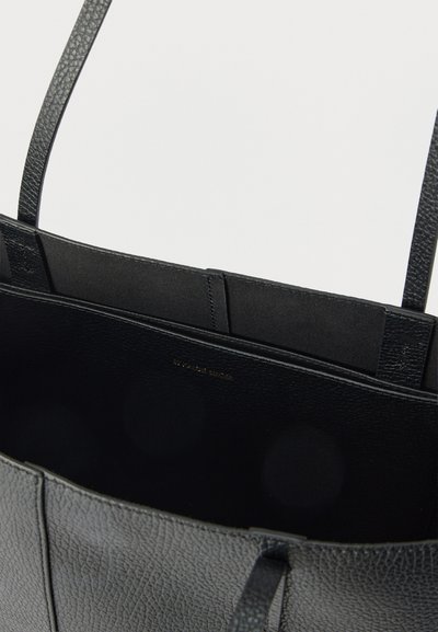 Μαύρη δερμάτινη τσάντα ώμου με ανάγλυφη υφή, λεπτές λαβές και ανοιχτό πάνω μέρος που αποκαλύπτει μια λεία εσωτερική επένδυση και δύο μικρές εσωτερικές τσέπες.