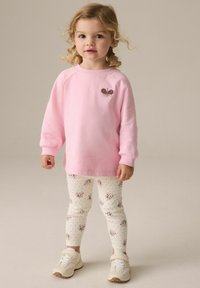Lyserød sweatshirt med en sommerfuglsbroderi, parret med hvide leggings med blomsterprint og polkaprikker. Hvide sneakers fuldender looket.