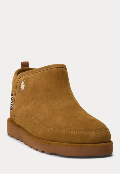 Brune ankelstøvler i semsket skinn med rund tå, lett tansåle i gummi og en bakre trekkstropp. Har en liten hvit logo på siden.