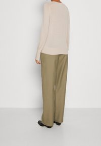 Beige leichtes Langarmoberteil mit Rundhalsausschnitt, kombiniert mit hellolivgrünen, weit geschnittenen Hosen und schwarzen Stiefeletten.