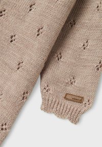 Strickschal in sanftem Beige mit kleinen Blattformen. Verfügt über einen gewellten Rand und ein braunes Lederetikett mit Markennamen.