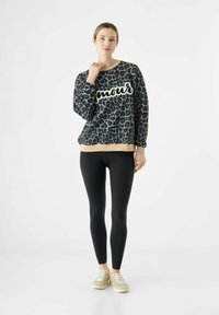 Sweater met luipaardprint en de tekst "amour" in crèmekleur, zwarte leggings en beige schoenen. Zacht materiaal, ronde halslijn, elastische boorden en zoom.