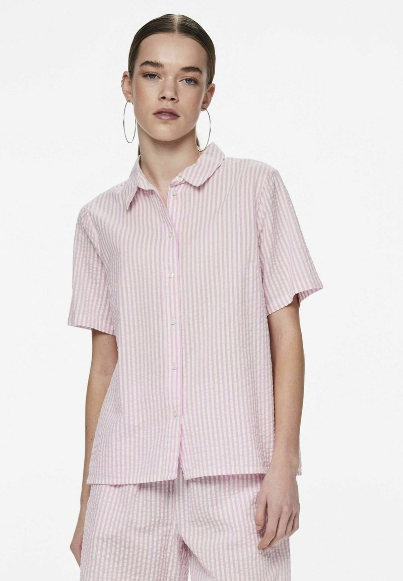 Camicia a maniche corte con bottoni in righe verticali rosa e bianche, con un colletto morbido e tessuto leggero. Accentuata da due bottoni.