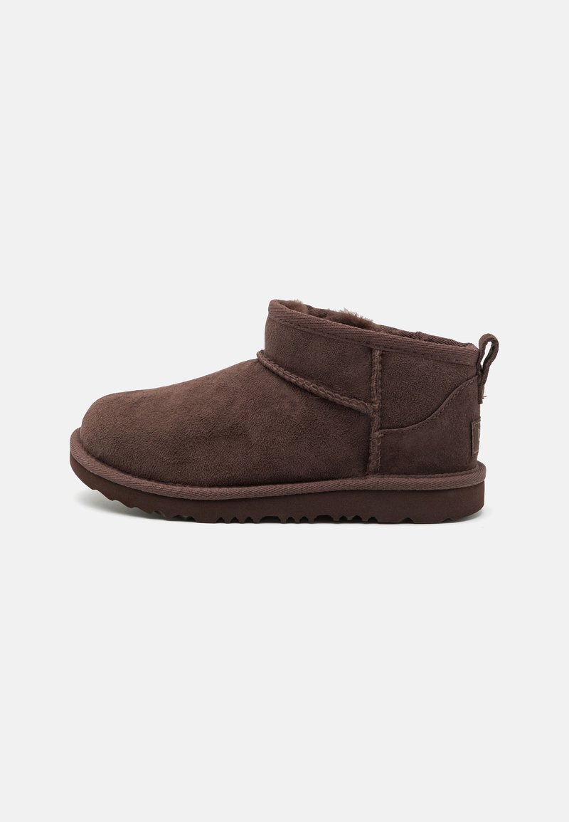 Botine din suede maro la nivelul gleznei, cu căptușeală din blană de oaie, vârf rotund, profil jos, cusături pe latură și un tab de prindere în spate. Talpă flexibilă.